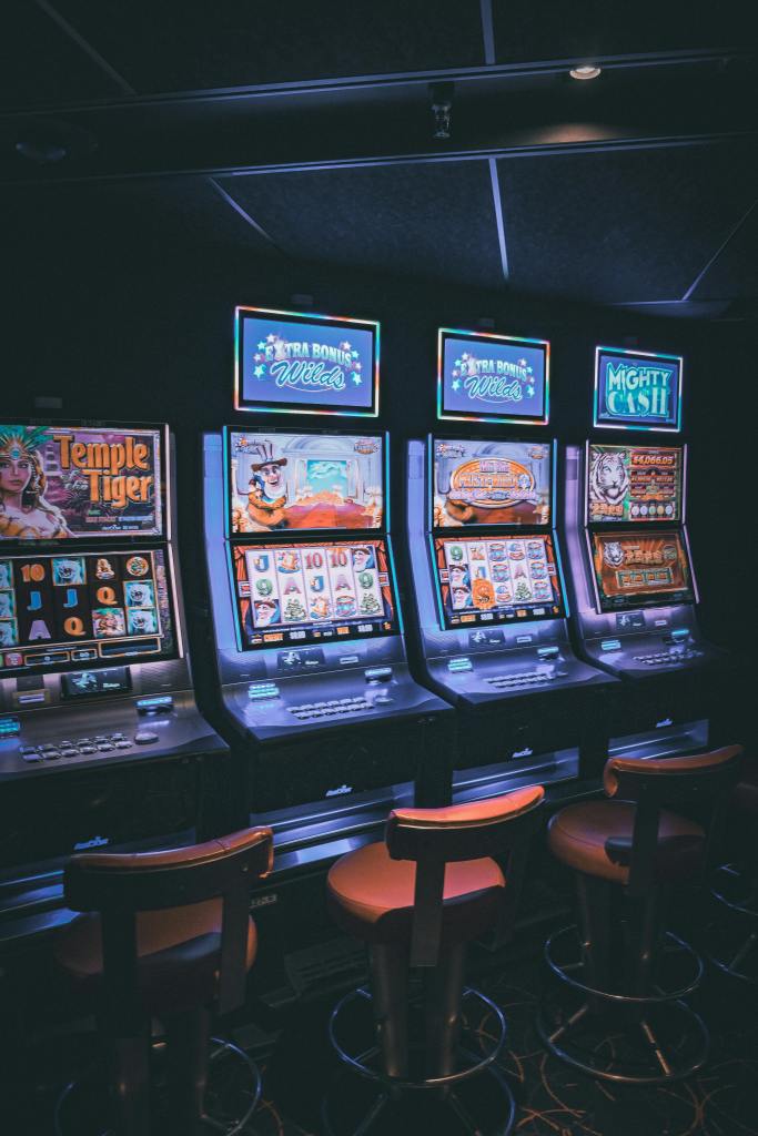 Four slot machines in a dim casino. Picture taken by Mathias Arseneau on Pexels.